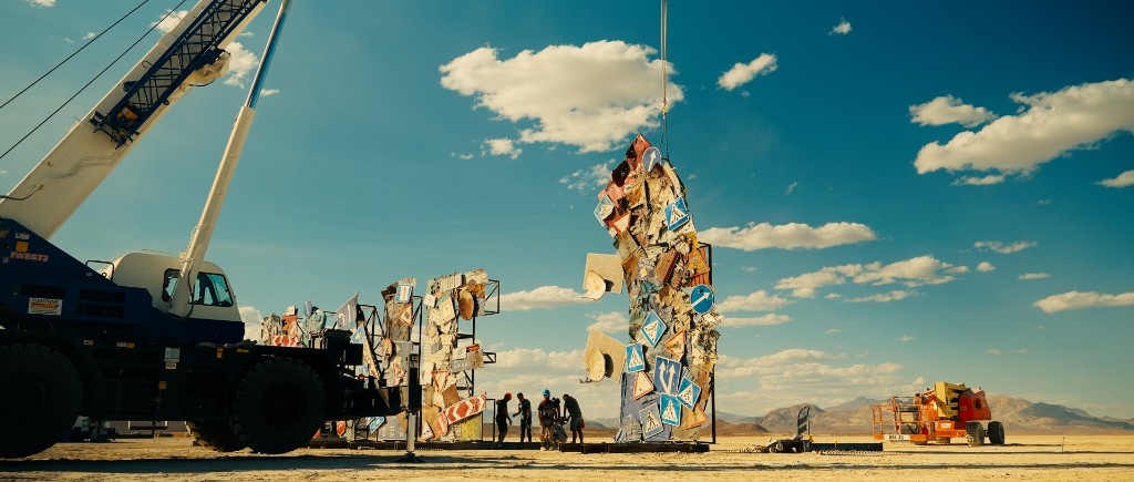 A crane lifts a metal-sign panel as artists assemble the WE'RE FINE installation in the Nevada desert